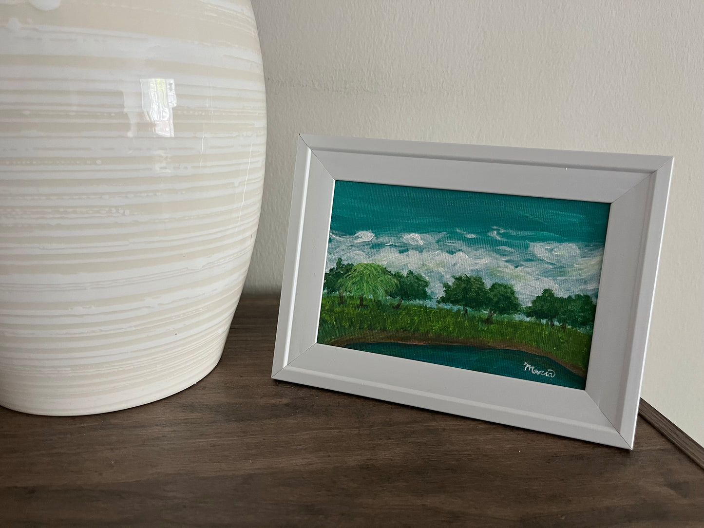 Framed pond painting in display next to vase